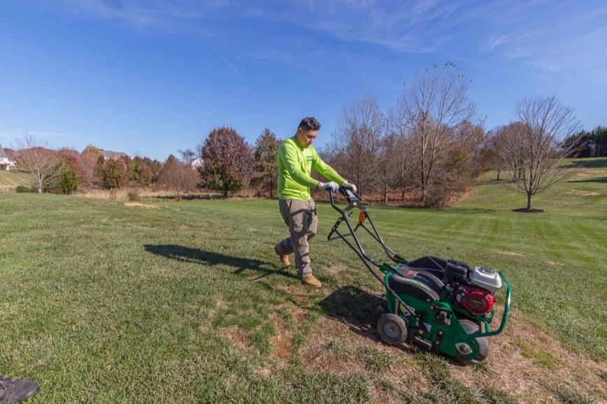AgroLawn technician running a core aerator across a lawn
