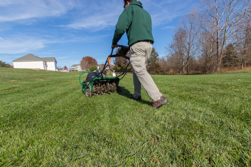 Lawn care technician running a walk-behind core aerator across a suburban lawn